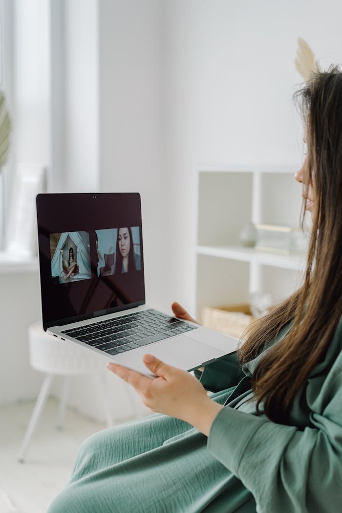 Woman using laptop for video call in a bright indoor setting.